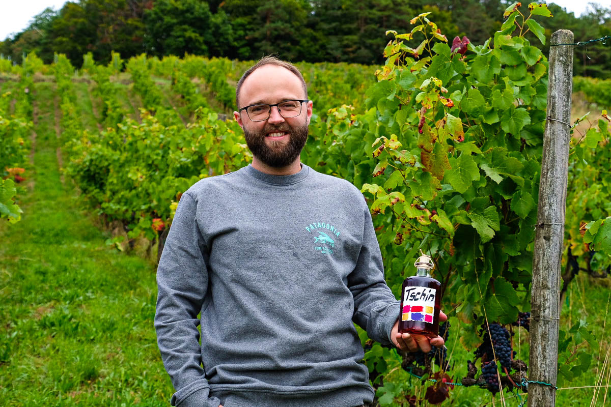 Raphael mit einem Tschin Pinot Noir in der Hand in den Reben